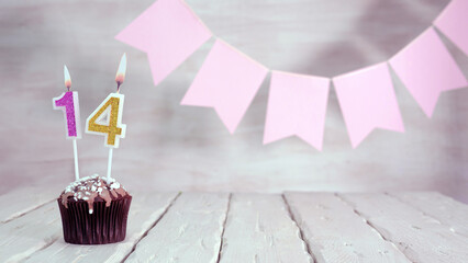Birthday number 14. Festive background for a girl or woman with a muffin and candles burning pink...
