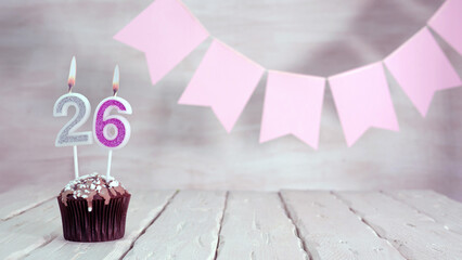 Birthday number 26. Festive background for a girl or woman with a muffin and candles burning pink...