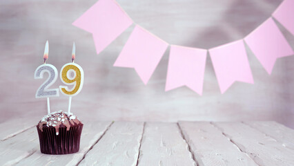 Birthday number 29. Festive background for a girl or woman with a muffin and candles burning pink...