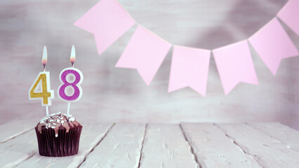 Birthday number 48. Festive background for a girl or woman with a muffin and candles burning pink...