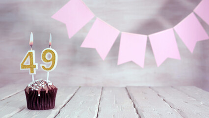 Birthday number 49. Festive background for a girl or woman with a muffin and candles burning pink...