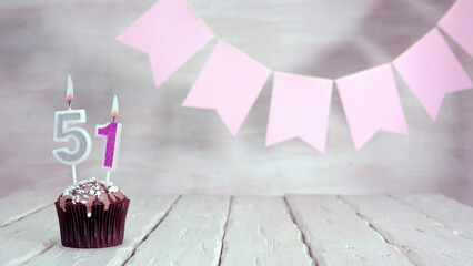 Birthday number 51. Festive background for a girl or woman with a muffin and candles burning pink...