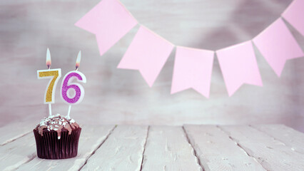 Birthday number 76. Festive background for a girl or woman with a muffin and candles burning pink...