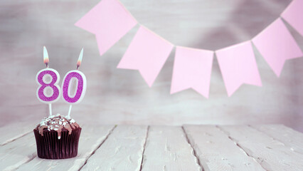 Birthday number 80. Festive background for a girl or woman with a muffin and candles burning pink...