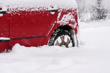 Red car parked in deep layer of snow after heavy snowstorm, detail to rear tire - only half wheel visible