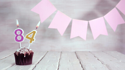 Birthday number 84. Festive background for a girl or woman with a muffin and candles burning pink...