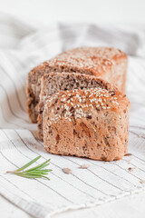 Sliced whole grain bread with sesame seeds on a light tablecloth with rosemary. Healthy eating concept. Gluten free bread.