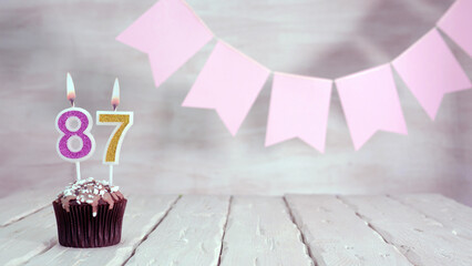 Birthday number 87. Festive background for a girl or woman with a muffin and candles burning pink...