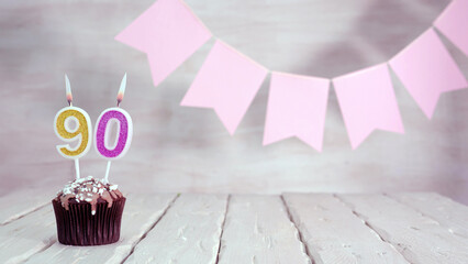 Birthday number 90. Festive background for a girl or woman with a muffin and candles burning pink...
