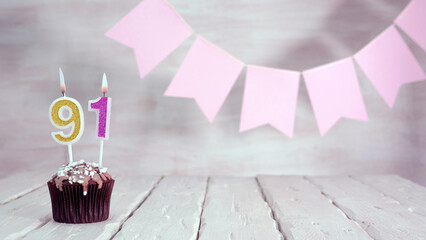 Birthday number 91. Festive background for a girl or woman with a muffin and candles burning pink...
