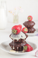 Freshly baked vegan chocolate muffins with red starwberries and white cream on a white plate. Gluten free dessert. Healthy breakfast concept.