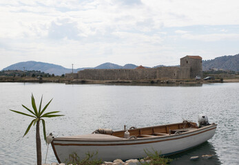 Fishing boat against which is the triangular fortress of Butrint in the Butrint National Park, Albania.