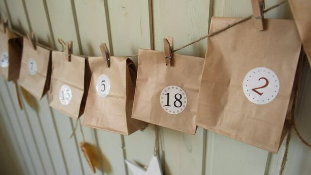 Advent calendar. Small handmade paper gifts hanging on the background of wooden wall, close up. Christmas Calendar, gift for children. DIY. Sustainable Christmas. Celebrating at home, childhood.