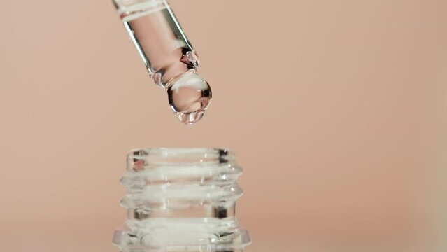 Dripping oil from pipette close-up, plant juice. Using aroma serum on pink background. Dropping liquid extract, skincare routine, treatment essence oil, spa concept. Traditional medicine