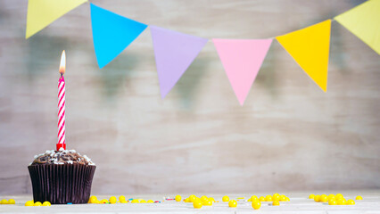 A muffin with a burning candle on the background of a garland of multi-colored mine space. Happy...