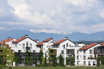 Fototapeta na wymiar Beautiful bungalows, covered with greenery, against the backdrop of mountains and snow-capped peaks. Urban landscape. A modern beautiful city. Sochi, Russia.