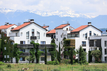Beautiful bungalows, covered with greenery, against the backdrop of mountains and snow-capped peaks. Urban landscape. A modern beautiful city. Sochi, Russia.