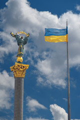 Monument of Independence in Kiev and ukrainian flag against blue sky with white clouds.