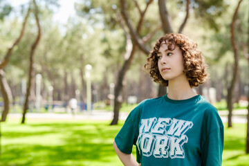 Young redhead woman wearing green t-shirt standing on city park, outdoor looking away with pensive face, dreaming, thinking over project tasks, problem solving. Copy space.
