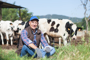 The farmer is resting in the meadow with his cows.