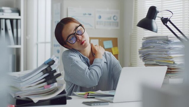 Tired Asian office employee massaging neck and shoulder muscles fatigued from using laptop computer for a long time, office syndrome concept