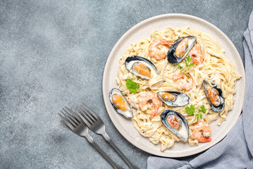 Pasta in a creamy sauce with seafood in a plate on a gray concrete background. Fettuccine with prawns and mussels. Top view, flat lay.