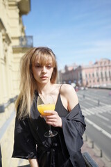 In the afternoon, in the light of the sun, a touching girl in black pajamas enjoys a glass of orange juice. She's good on the balcony.