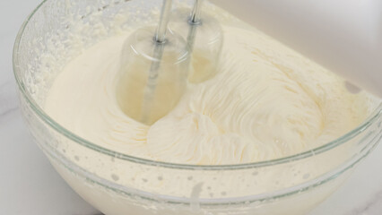 Whipped cream cheese desert recipe. Mixing ingredients in a glass bowl using an electric mixer, close up cooking process, marble background with copy space, flat lay