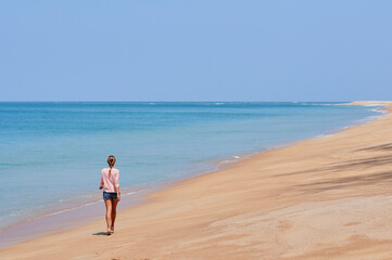 Vacation on the shore. Young woman walking on tropical beach enjoying beautiful view.