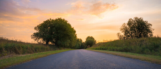 Fototapeta premium country road among meadows colorful sunset on background