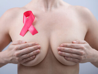 Pink breast cancer awareness ribbon on the chest of a naked woman on a white background.