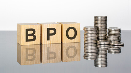 bpo - text on wooden cubes on a cold grey light background with stacks coins