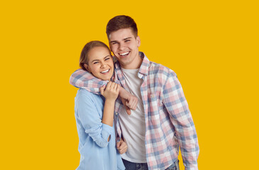Happy beautiful romantic teenage couple. Older brother and sister with toothy smiles. Handsome Caucasian man and young woman in shirts standing in studio, hugging each other, sharing positive emotions