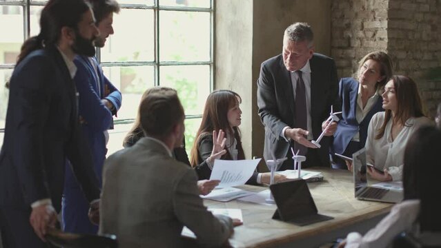 senior businessman with miniature windmill in hand talking to multiethnic group business colleagues in office