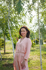 Woman in pink dress standing among green birch trees.