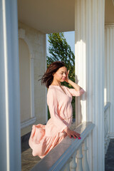 Woman in pink dress with hair flying on wind standing on stairs outdoors