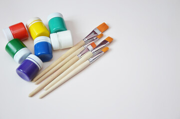 Jars of gouache paint in different colors and synthetic brushes. A set of objects for drawing....