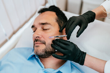 Handsome middle age bearded man is getting a rejuvenating facial injections at beauty clinic. The...