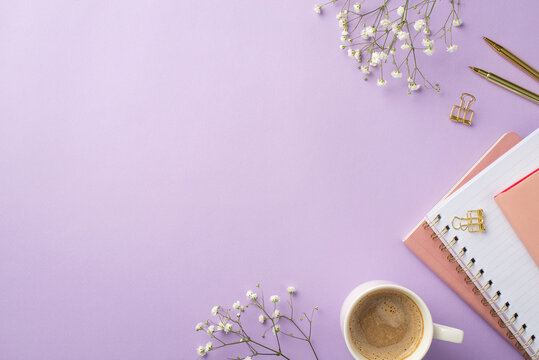 Business concept. Top view photo of workplace stationery gold pens binder clips stack of pink diaries cup of coffee and white gypsophila flowers on isolated lilac background with empty space