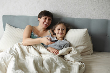 happy mother with daughter in bed watching tv