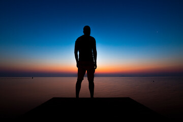 Silhouette of young man on a jetty in front of the Mar Menor, in the Region of Murcia, Spain, in a colorful sunset