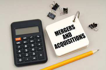 On a gray surface, a calculator, a pencil and a notepad with the inscription - Mergers and...