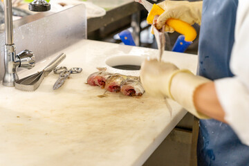 Unrecognizable fishmonger cutting fish with a knife on a white table next to the cutting utensils. High quality photo