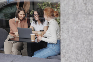 three female colleagues or students are working on a laptop and discussing a project or creative...