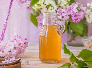 Lilac flavored sugar syrup for lemonades, ice cream or biscuits in a glass bottle on a light wooden background.