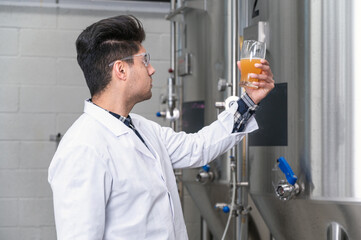 Brewer wearing white coat controlling process of beer fermentation while working at modern beer factory. High quality photography