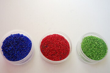 Three Circular Boxes of Blue, Red and Green Glass Beads on White Canvas Background