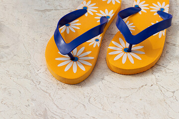 Yellow women's beach slippers with a pattern of flowers on a stone background. National flip flops...