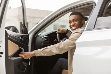 Smiling man sitting in the car, getting in or out of the car, holding the door open, looking at the...