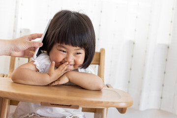 母親の持つスマートフォンで電話をする赤ちゃん（1歳10か月、女の子、日本人）